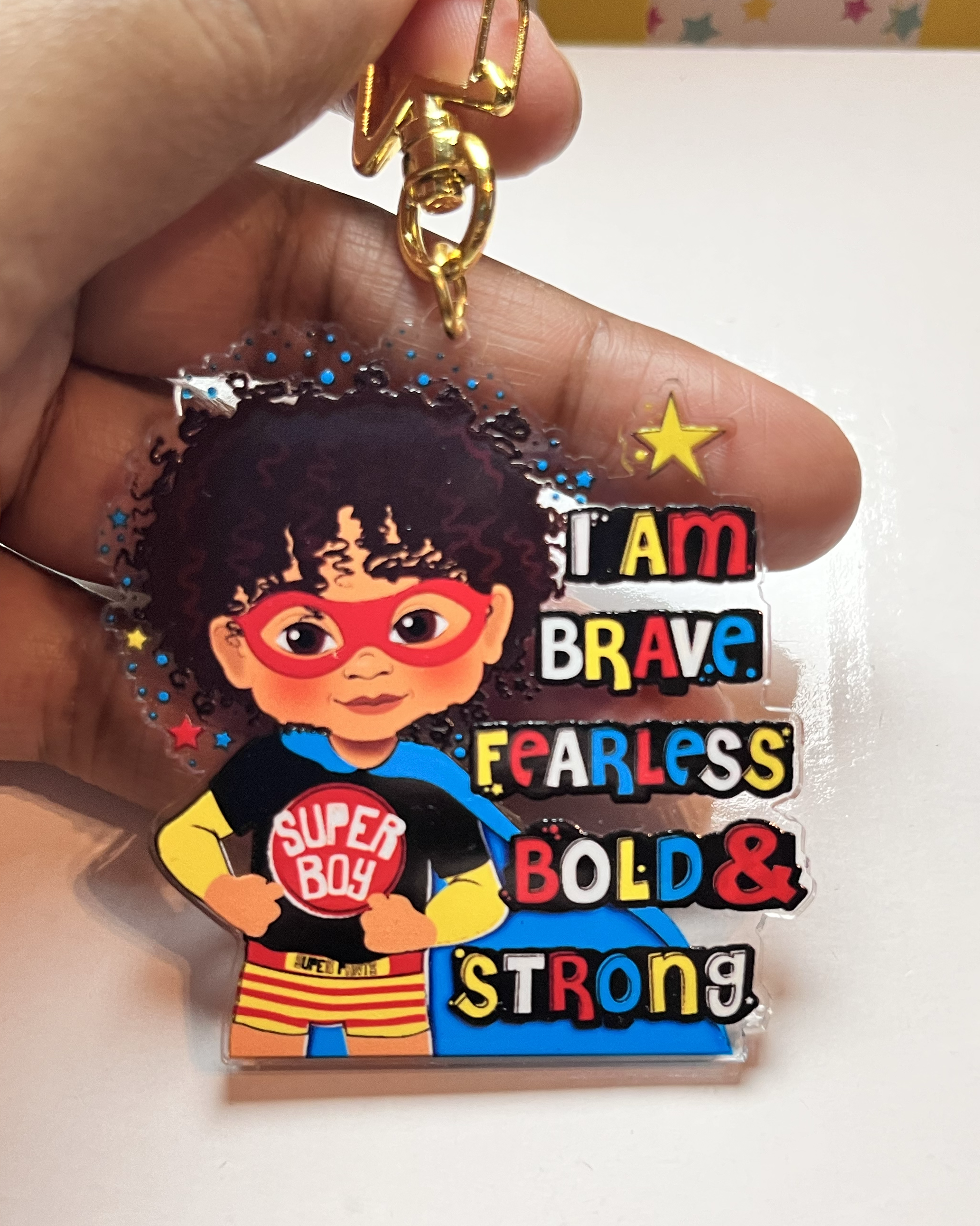 Keychain with brown boy superhero design and motivational text held by a hand.