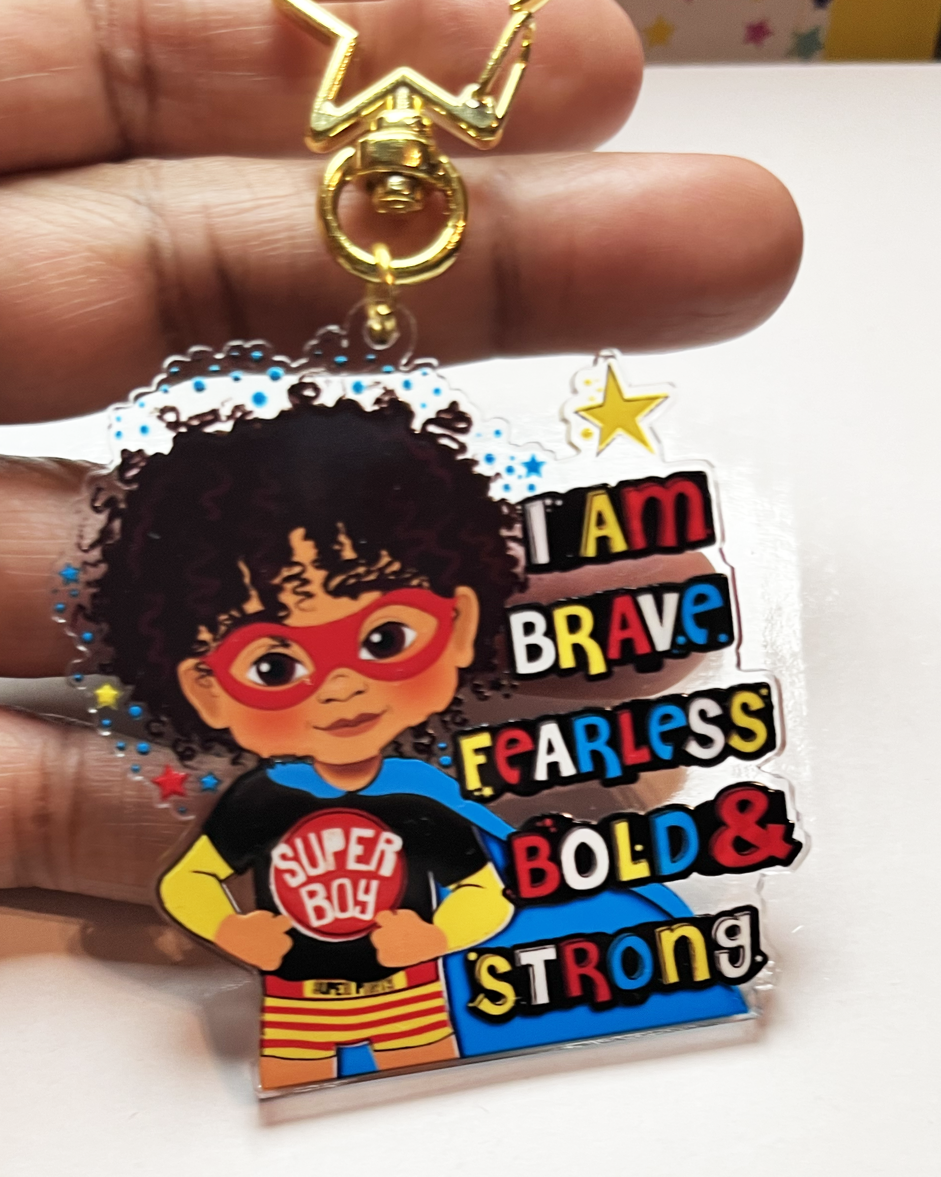 Superhero-themed keychain with a mixed race boy character and motivational text held by a hand.