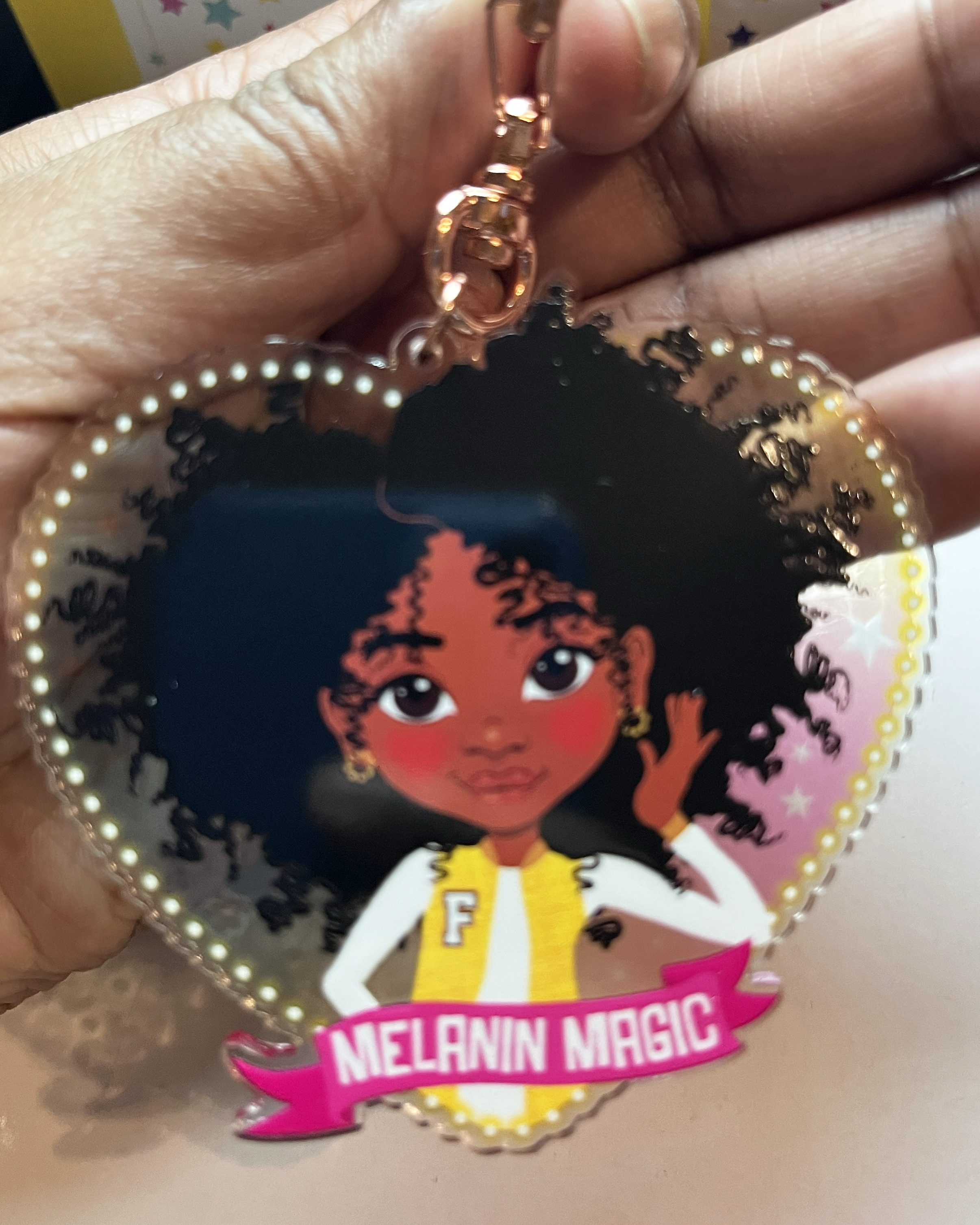 Heart-shaped keychain with a Black Afro Girl hand drawn character and 'Melanin Magic' text on a banner scroll. Black tween / teen Girl keyring with curly afro and “Melanin Magic” affirmation