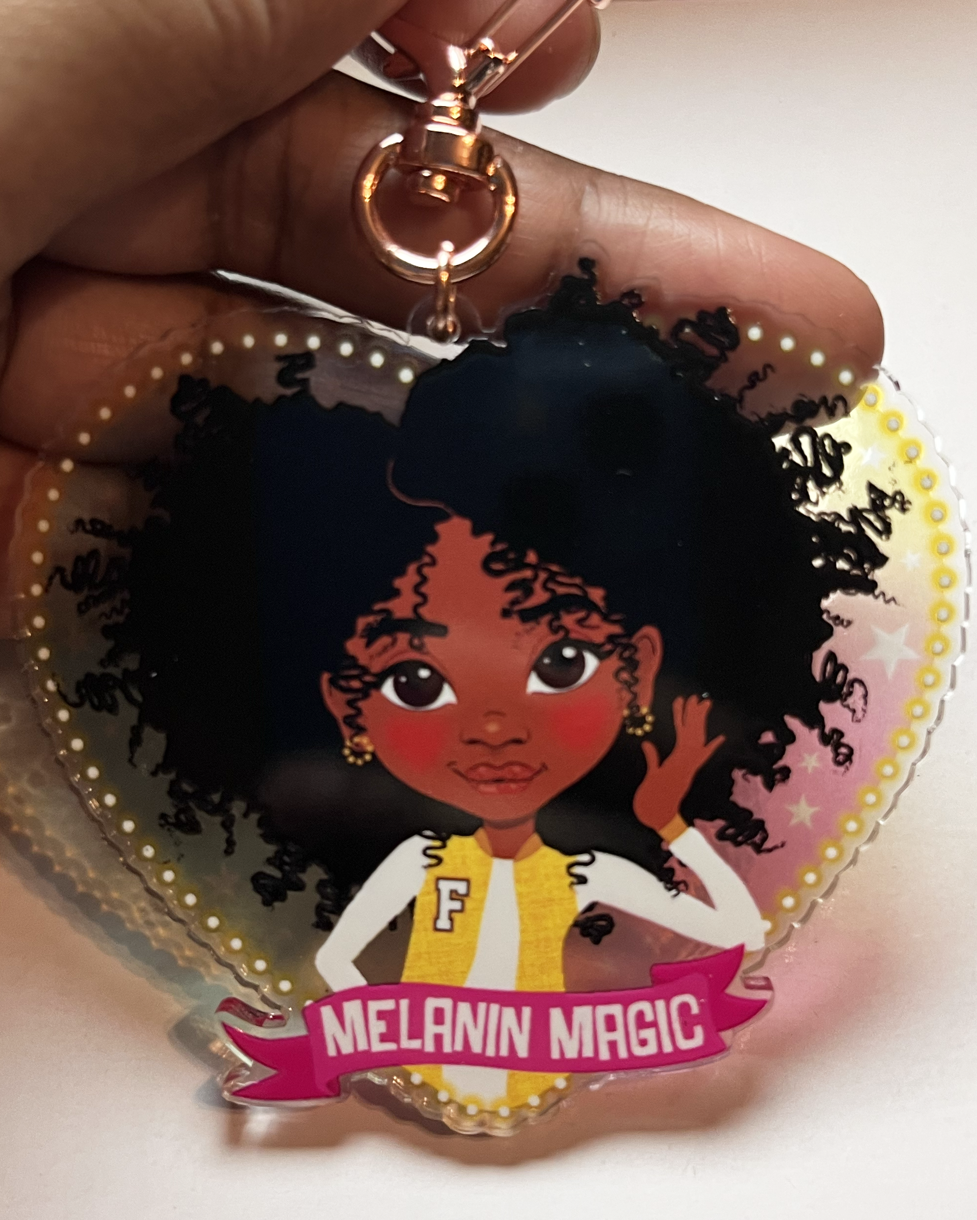 Heart-shaped keychain with illustration of a black girl and 'Melanin Magic' text, held by a hand.