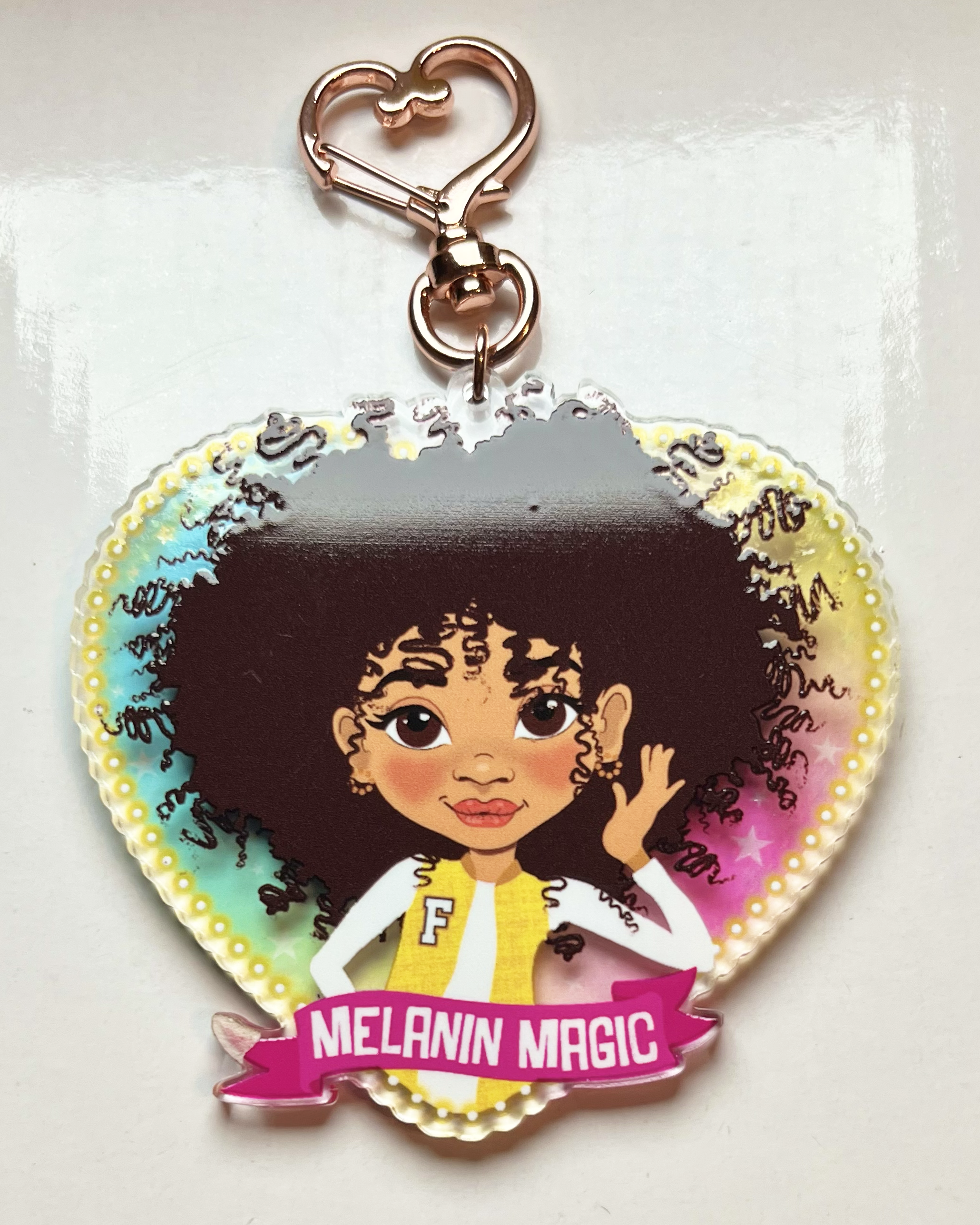 Heart-shaped keychain with a Mixed race Afro Girl hand drawn character and 'Melanin Magic' text on a banner scroll. Brown tween / teen Girl keyring with curly afro and “Melanin Magic” affirmation