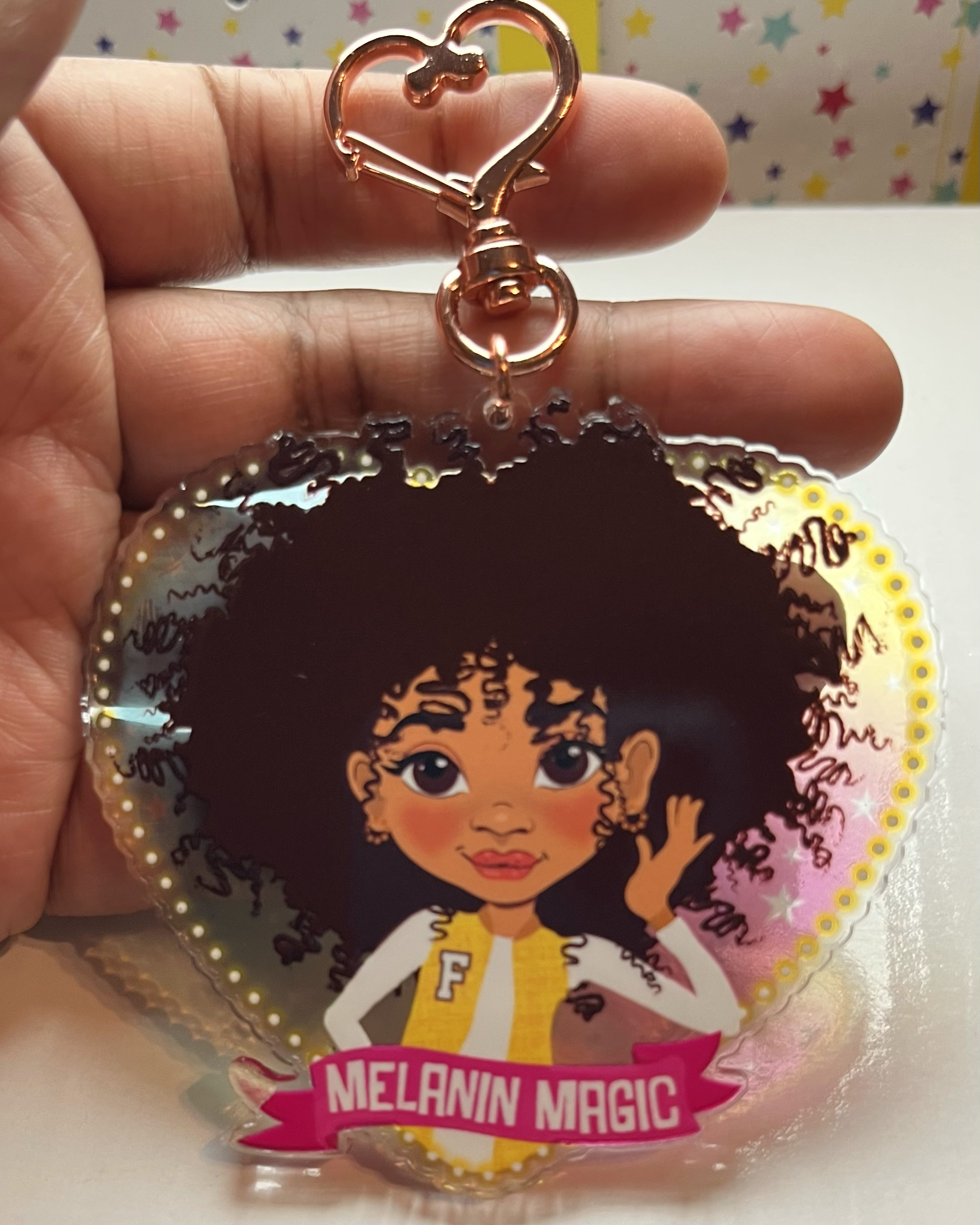 Heart-shaped keychain with illustration of a brown girl and 'Melanin Magic' text, held by a hand.