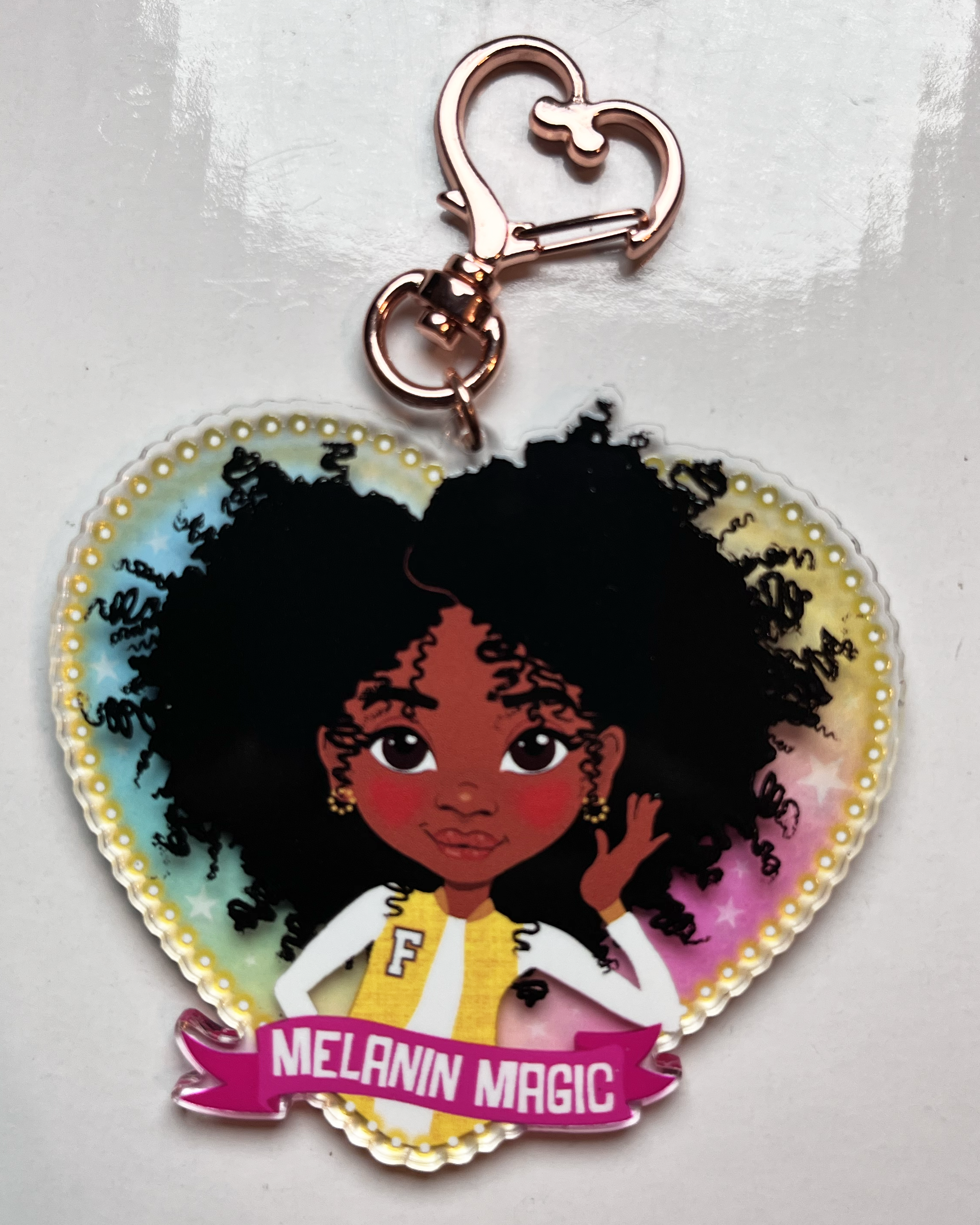 Heart-shaped keychain with a black girl character and 'Melanin Magic' text on a transparent rainbow background
