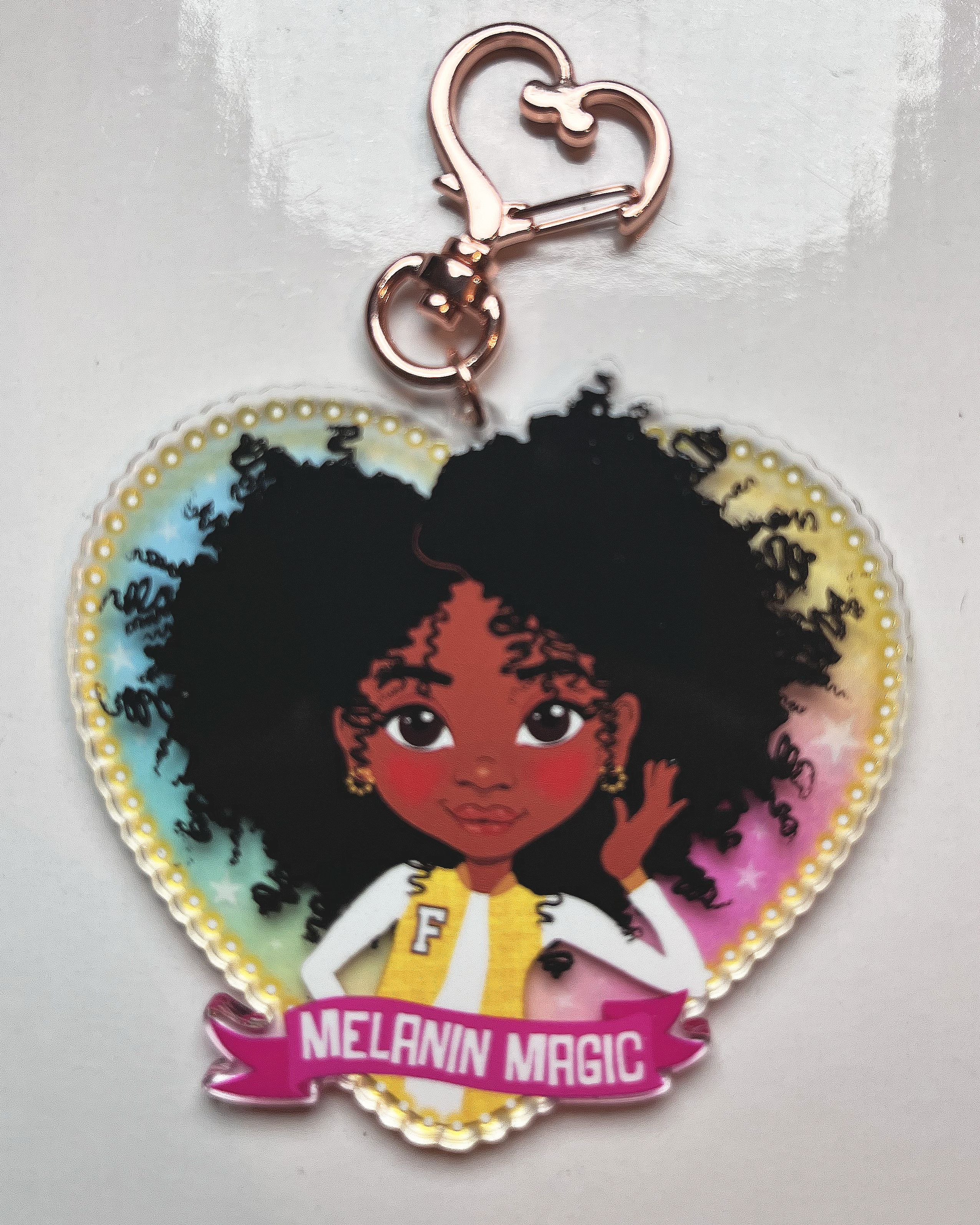 Heart-shaped keychain with a cartoon character and 'Melanin Magic' text on a transparent rainbow glazed  background
